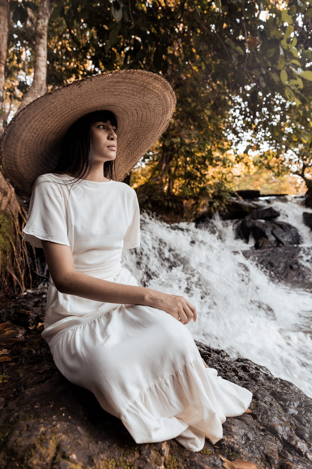 woman in white dress wearing brown straw hat sitting on rock