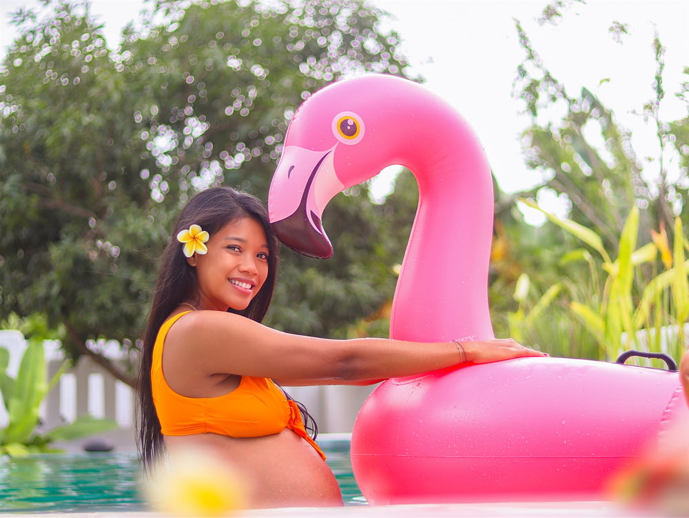 woman in orange bikini top holding pink inflatable flamingo