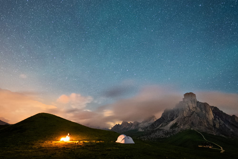 white tent on green grass field near mountain under blue sky with stars during night time