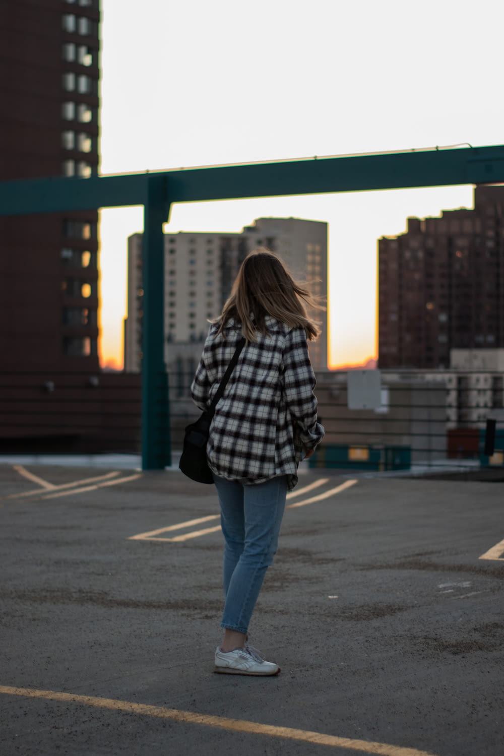 woman in black and white plaid shirt and blue denim jeans standing on sidewalk during daytime