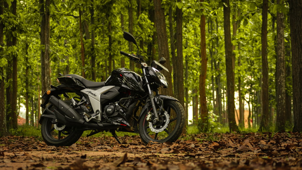 Moto noire et argentée garée sur un chemin de terre brun dans la forêt pendant la journée