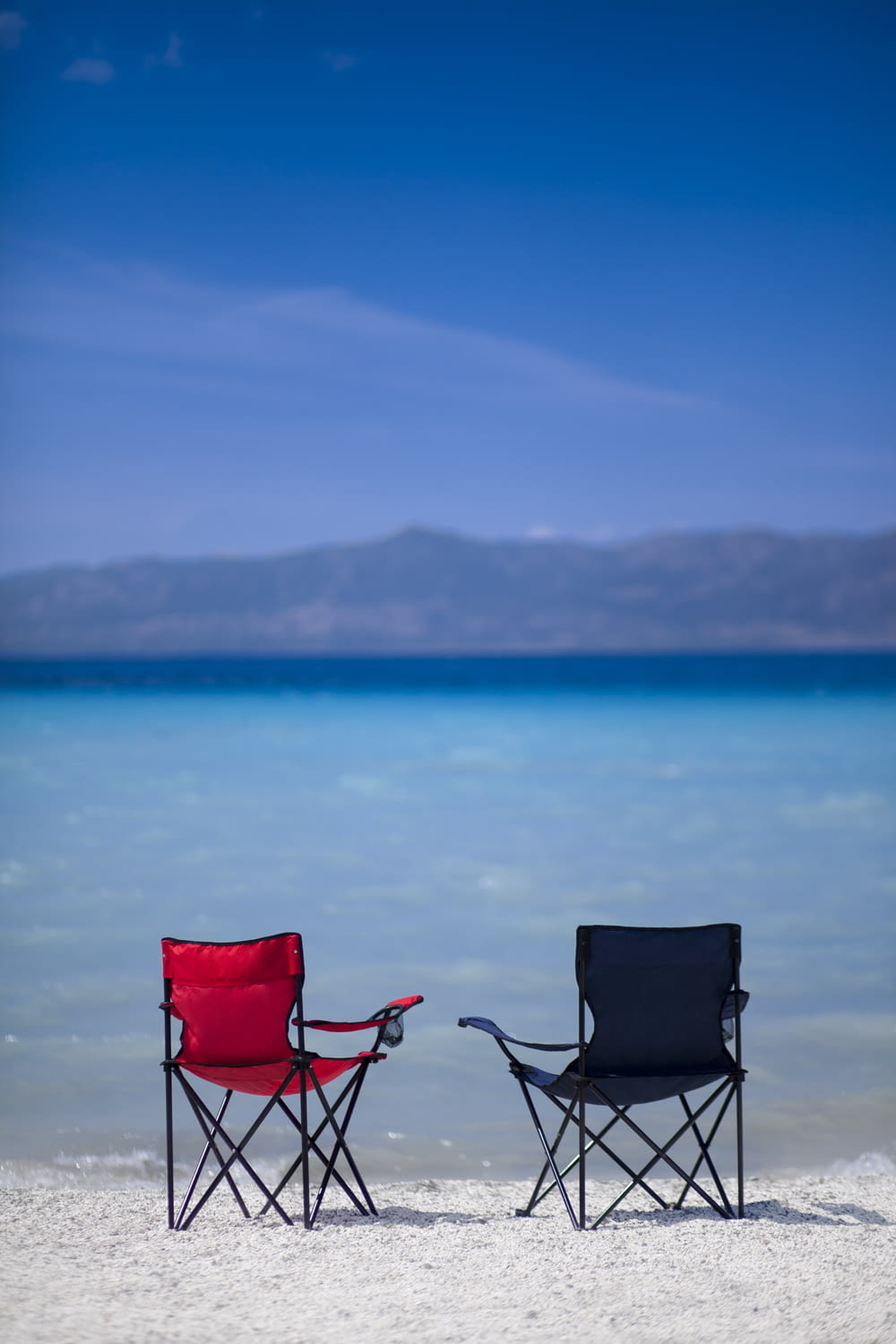 Chaise de camping rouge et noire sur le sable gris près du plan d’eau pendant la journée