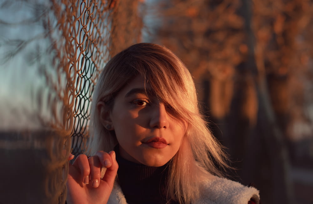 woman in gray sweater leaning on gray metal fence during daytime