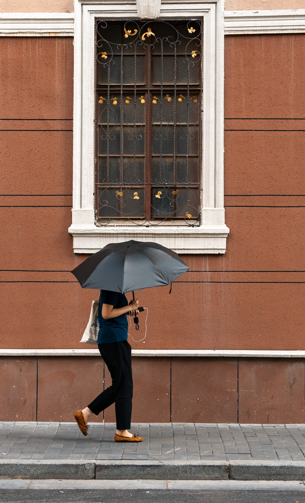 woman in black coat holding umbrella standing in front of brown concrete building