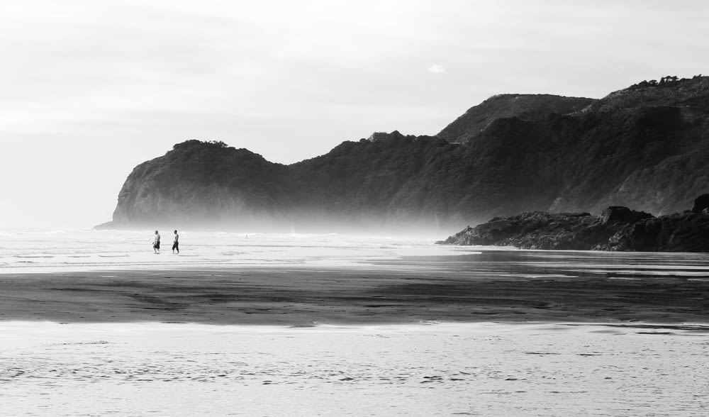 grayscale photo of 2 people walking on beach