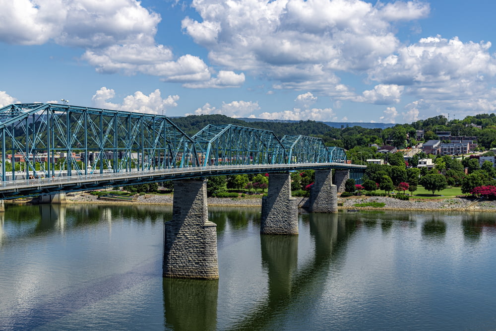 green metal bridge over river under blue sky and white clouds during daytime