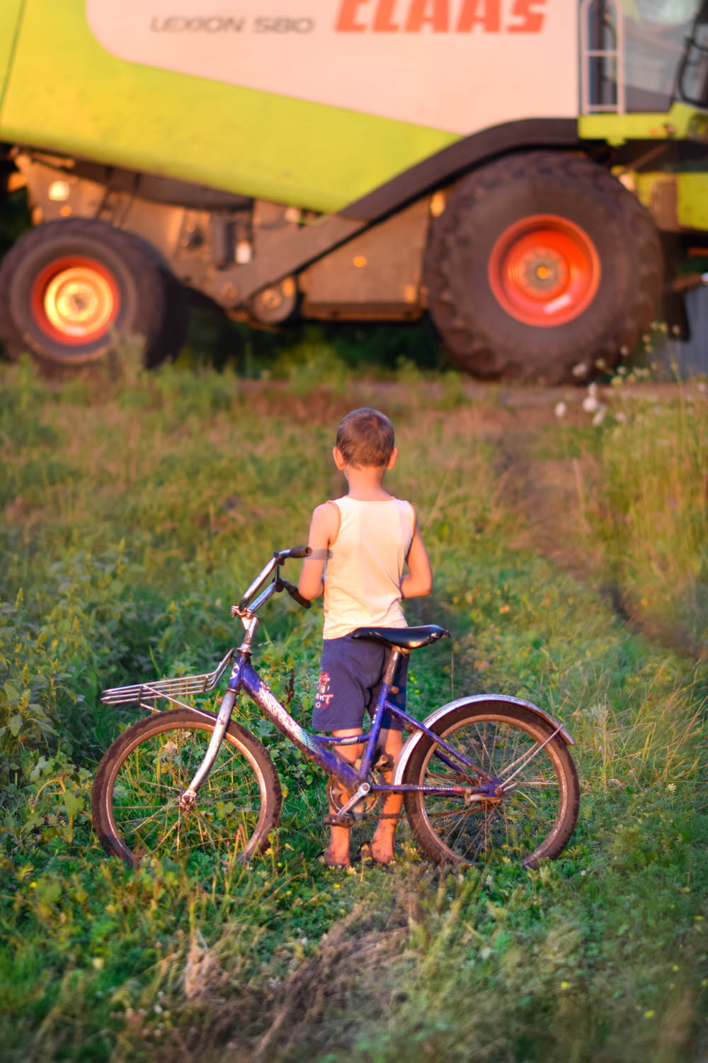 Ein kleiner Junge steht neben einem Fahrrad auf einem Feld