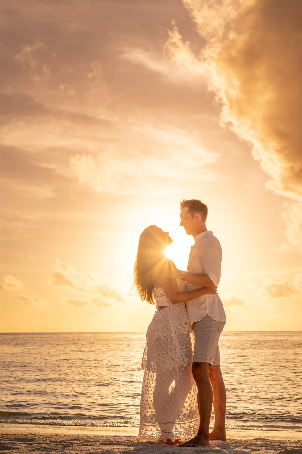 uomo e donna che si baciano sulla spiaggia durante il tramonto