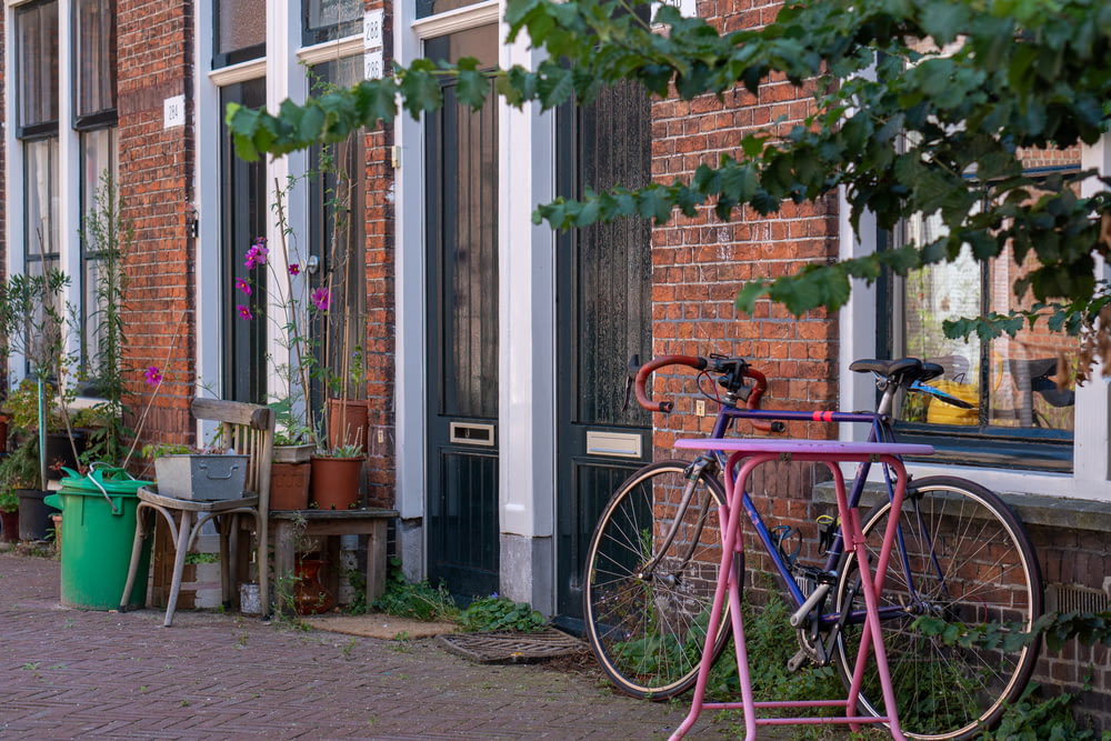 Bicicleta roja de la ciudad estacionada junto a un edificio de concreto verde y marrón durante el día