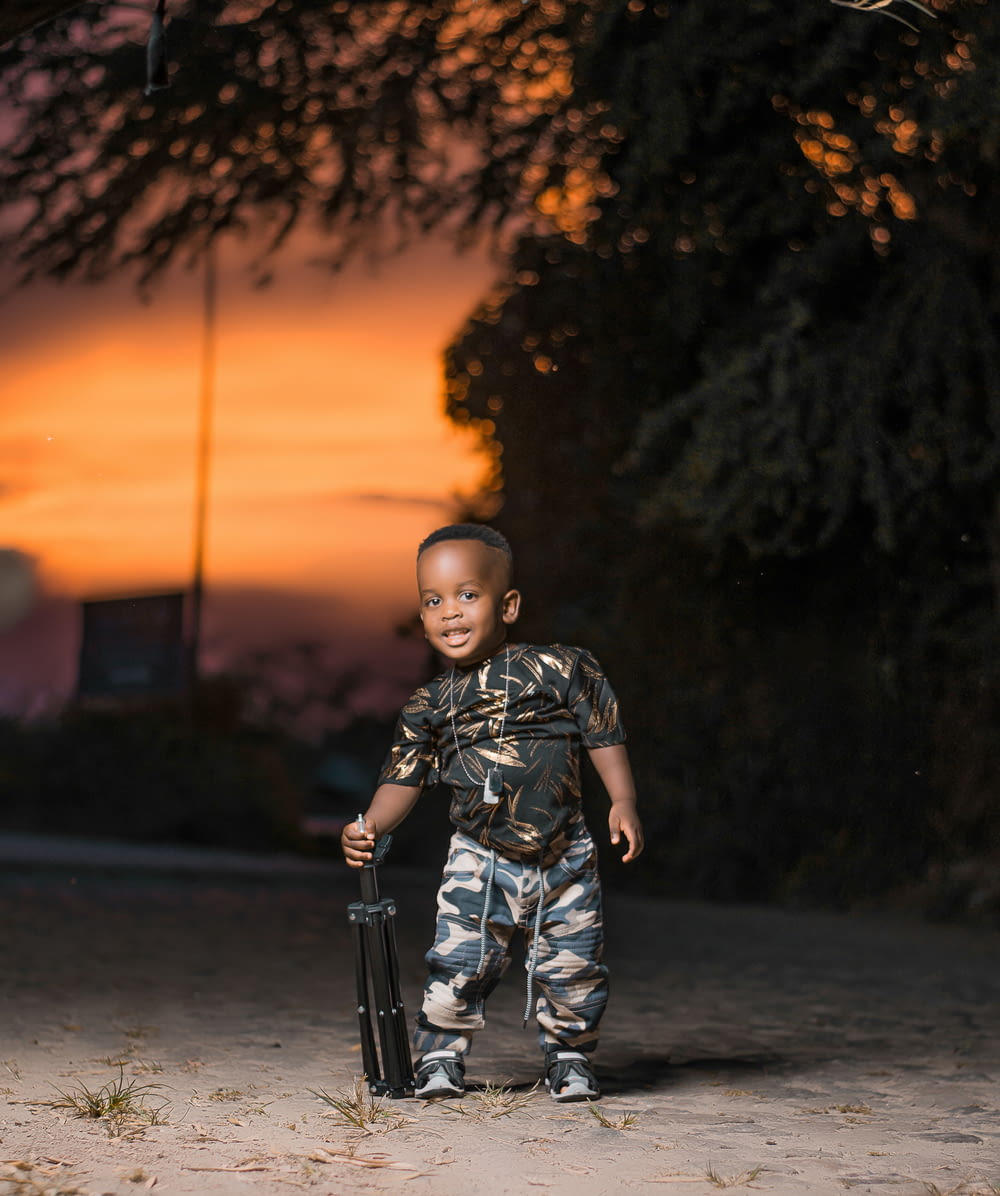 boy in black and white camouflage jacket standing on road during sunset