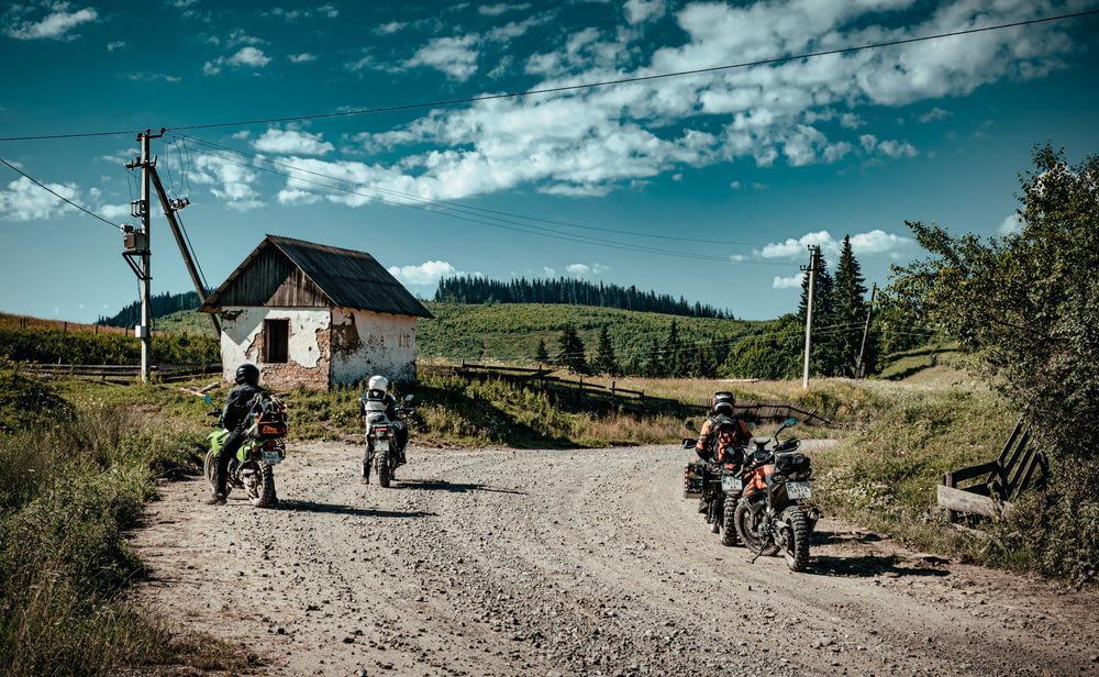 people riding motorcycle on road near green trees and brown wooden house during daytime