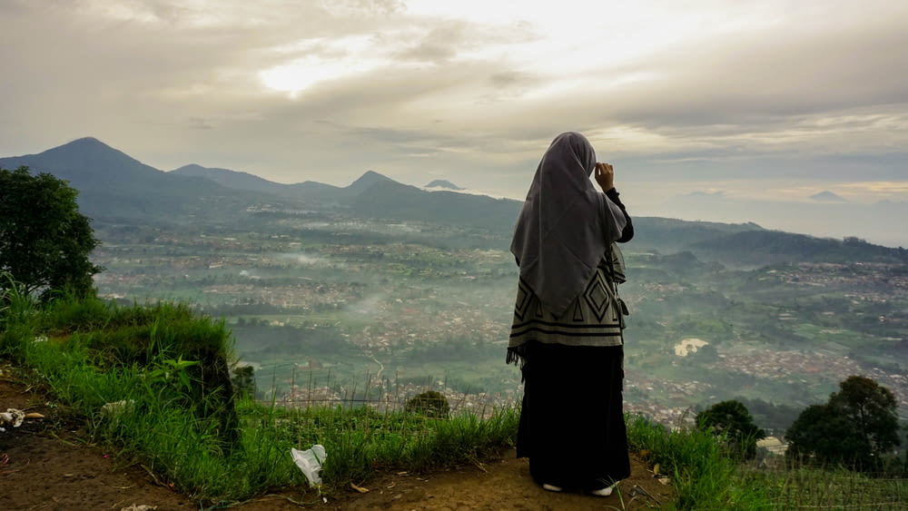 Mujer con hiyab blanco y negro de pie en un campo de hierba verde durante el día