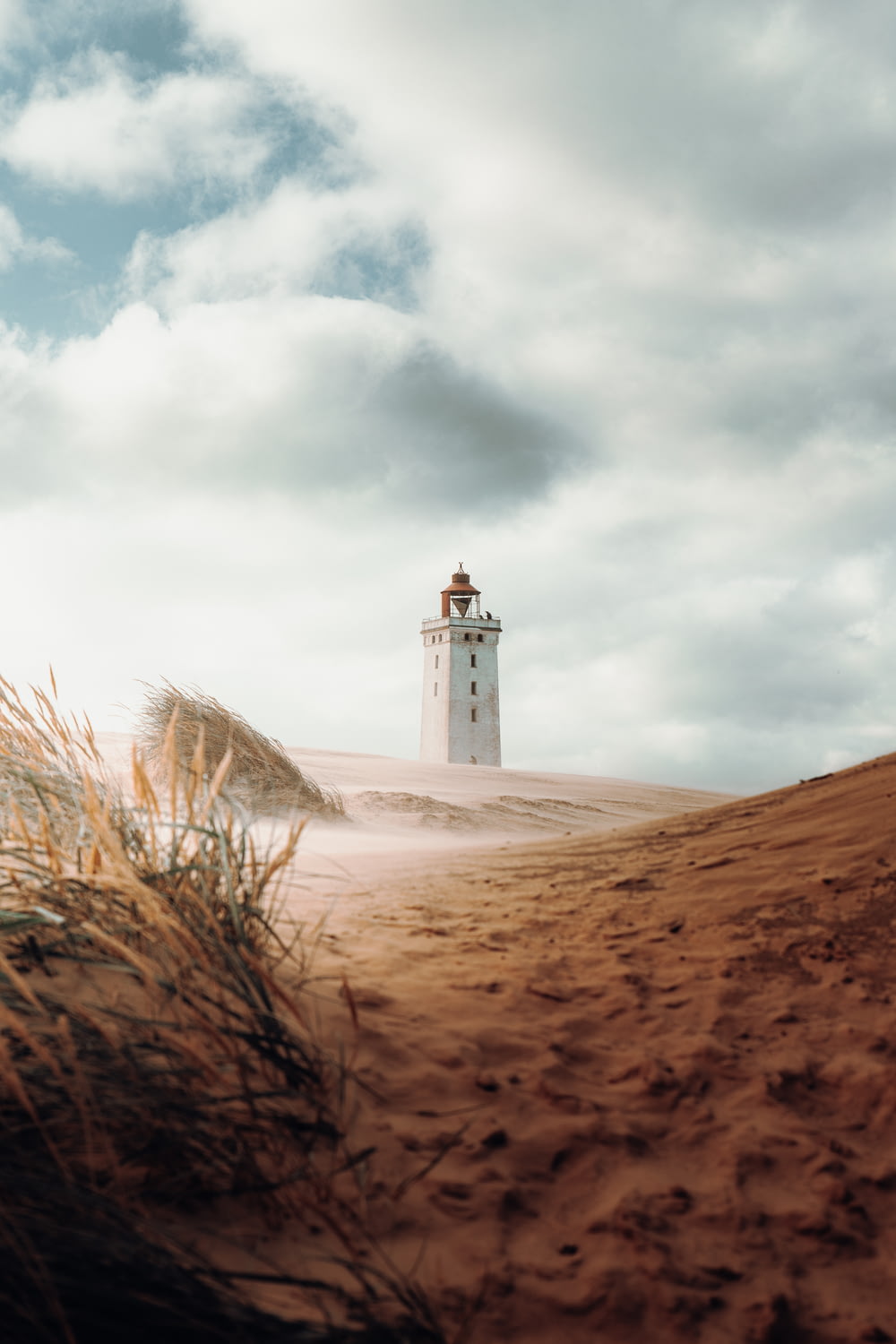 white concrete lighthouse on brown sand under white clouds during daytime