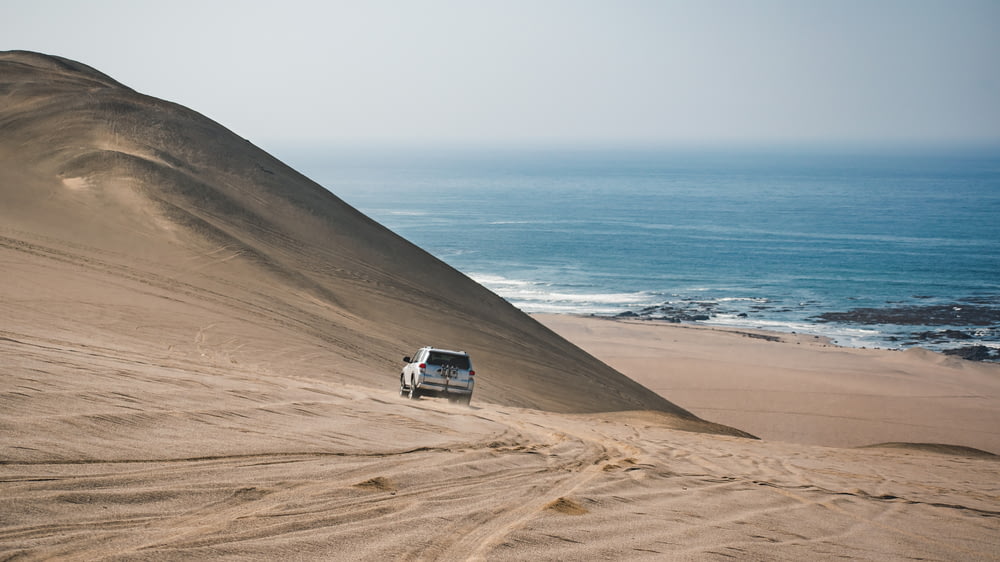 white car on brown sand near body of water during daytime