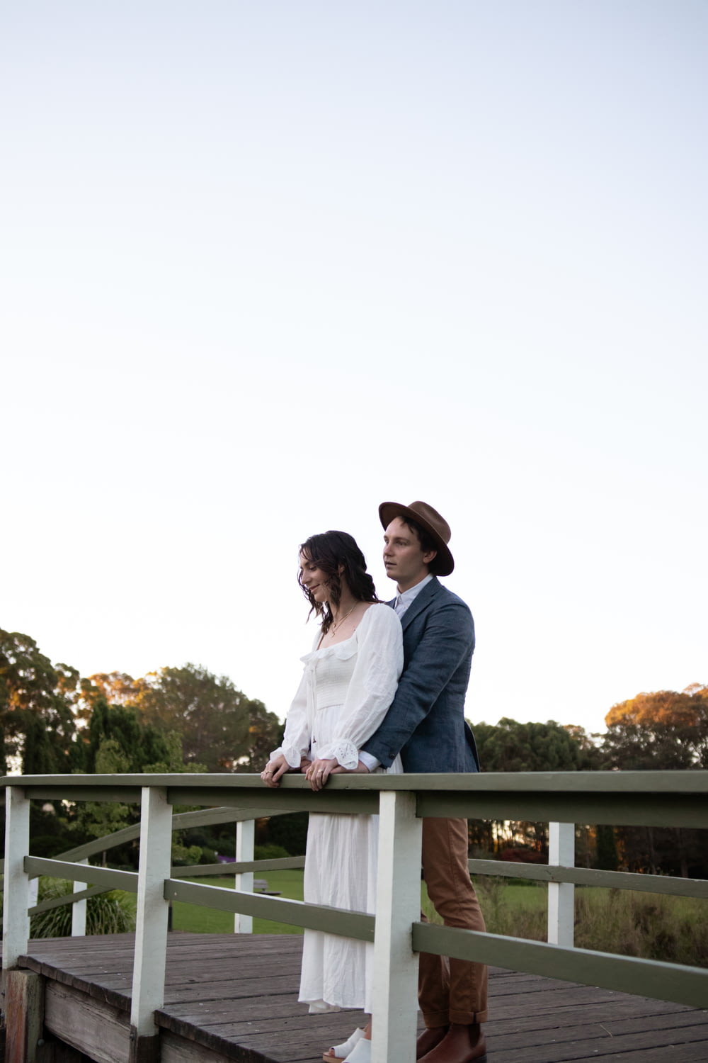 man in white dress shirt and woman in white dress standing on white wooden bridge during
