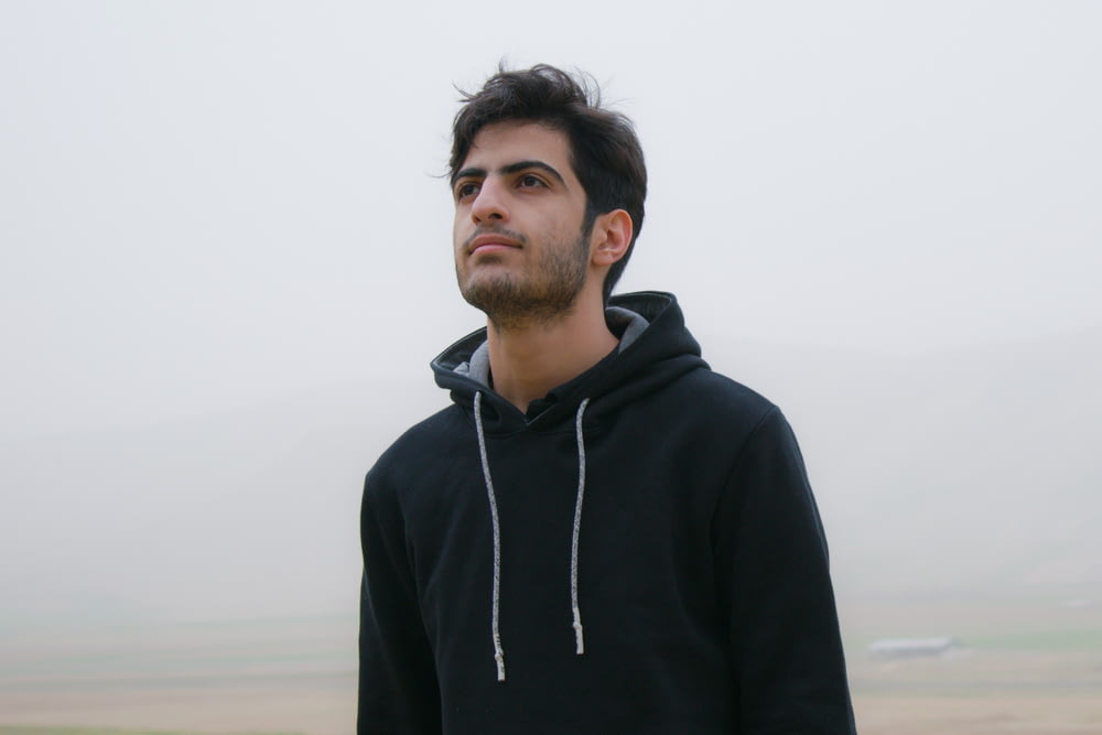 um homem em um capuz preto de pé em um campo nebuloso