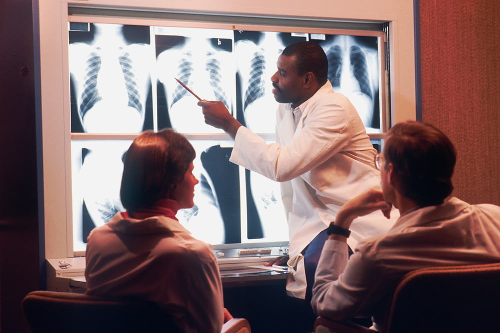 um homem em um jaleco branco apontando para um raio-x
