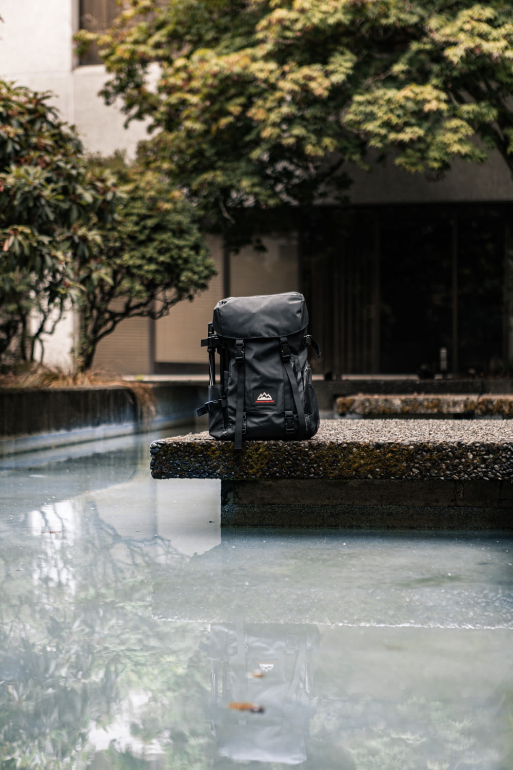 a black backpack sitting on a ledge next to a body of water
