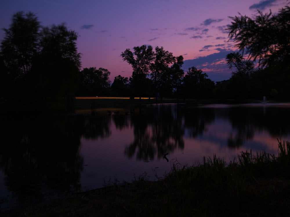 a lake with a purple sky and trees in the background