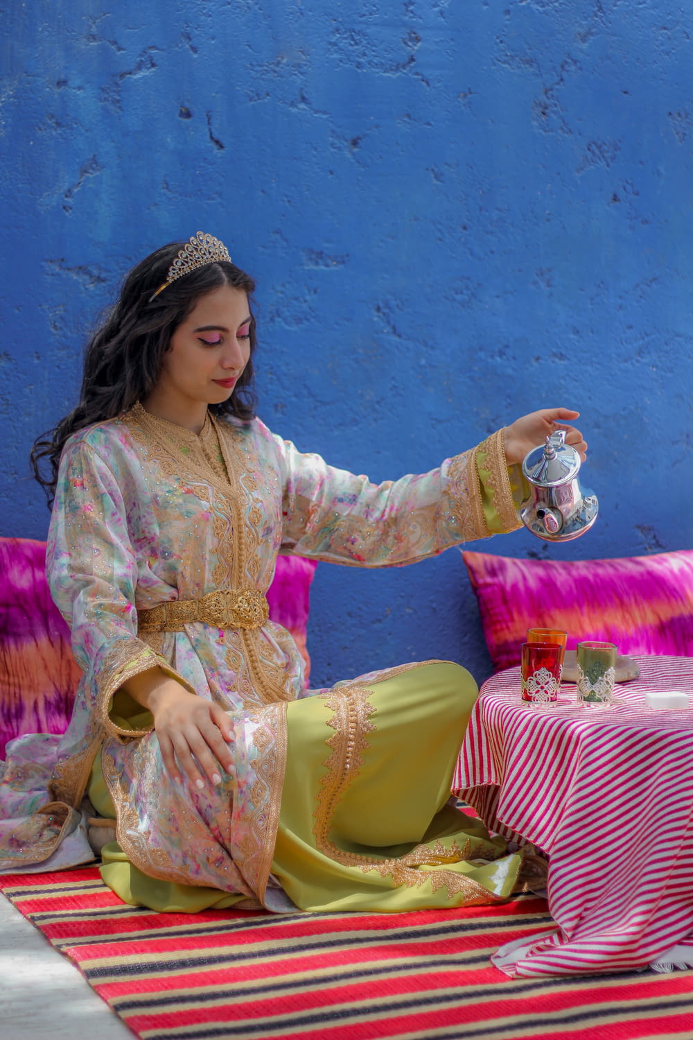 a woman sitting on the ground holding a tea pot