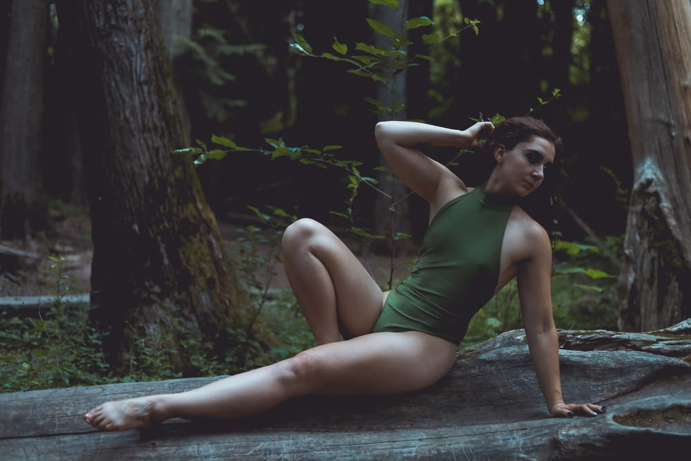 a woman in a green bodysuit sitting on a rock in the woods