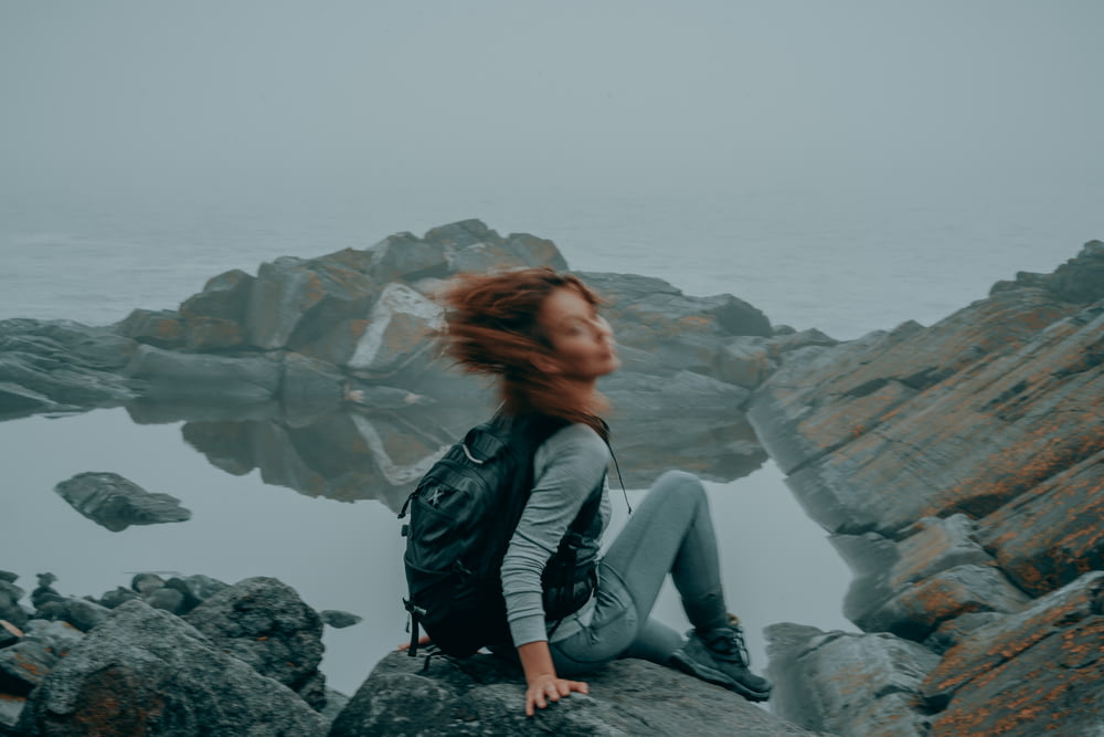 uma mulher com cabelo ruivo sentada em uma rocha à beira do oceano