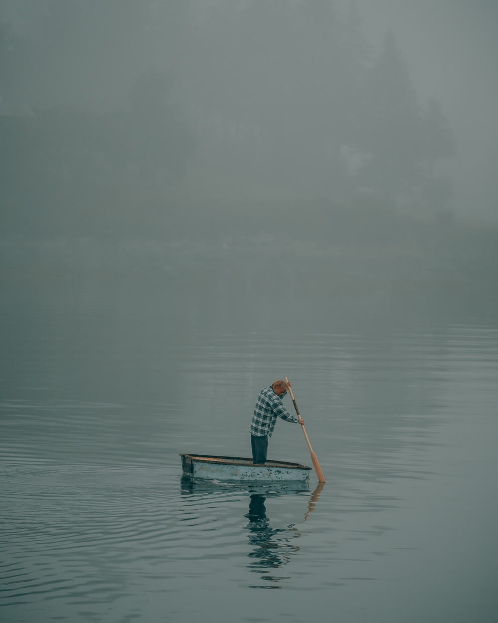 um homem remando um barco em um lago nebuloso