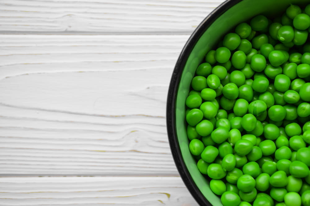 a green bowl filled with peas on top of a white table