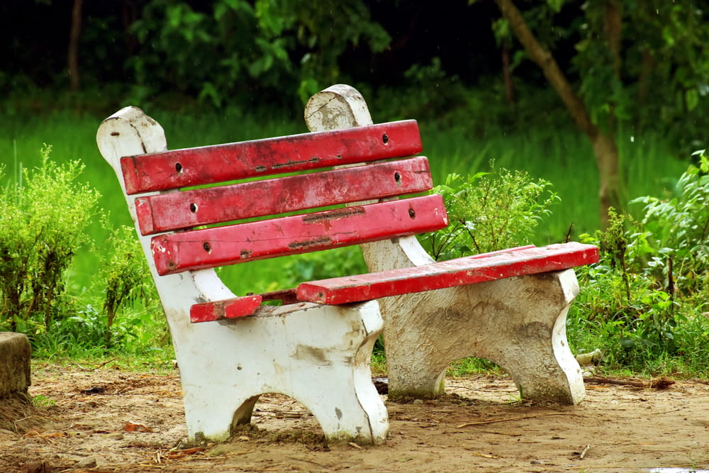 a red and white bench sitting on top of a dirt field