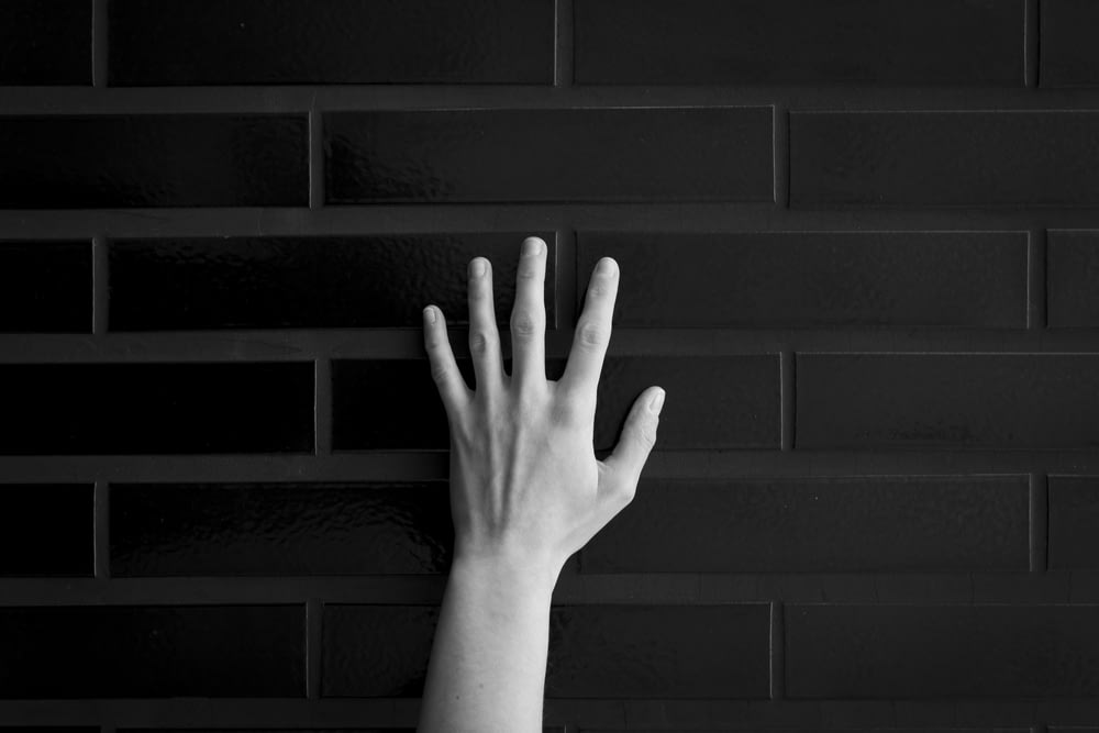 a hand reaching up against a black brick wall