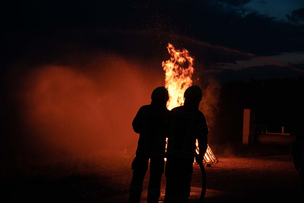 two people standing in front of a fire