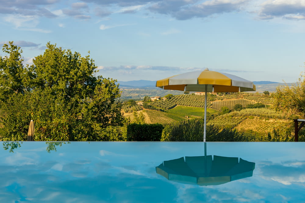 an umbrella sitting on top of a pool next to a lush green hillside