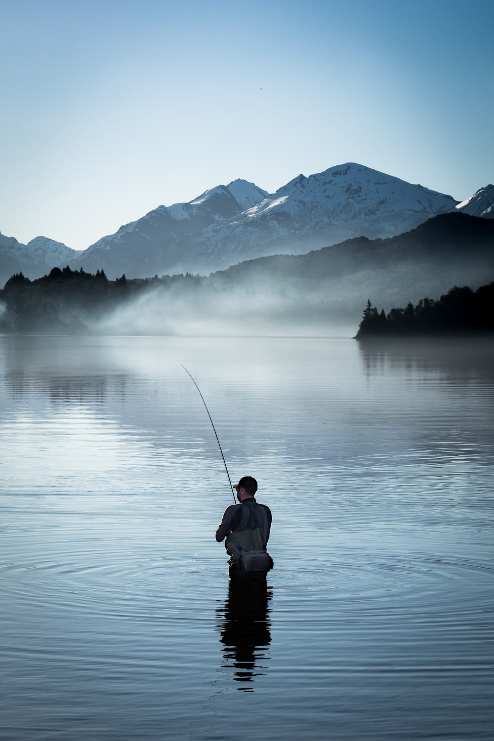 a man standing in a body of water holding a fishing pole
