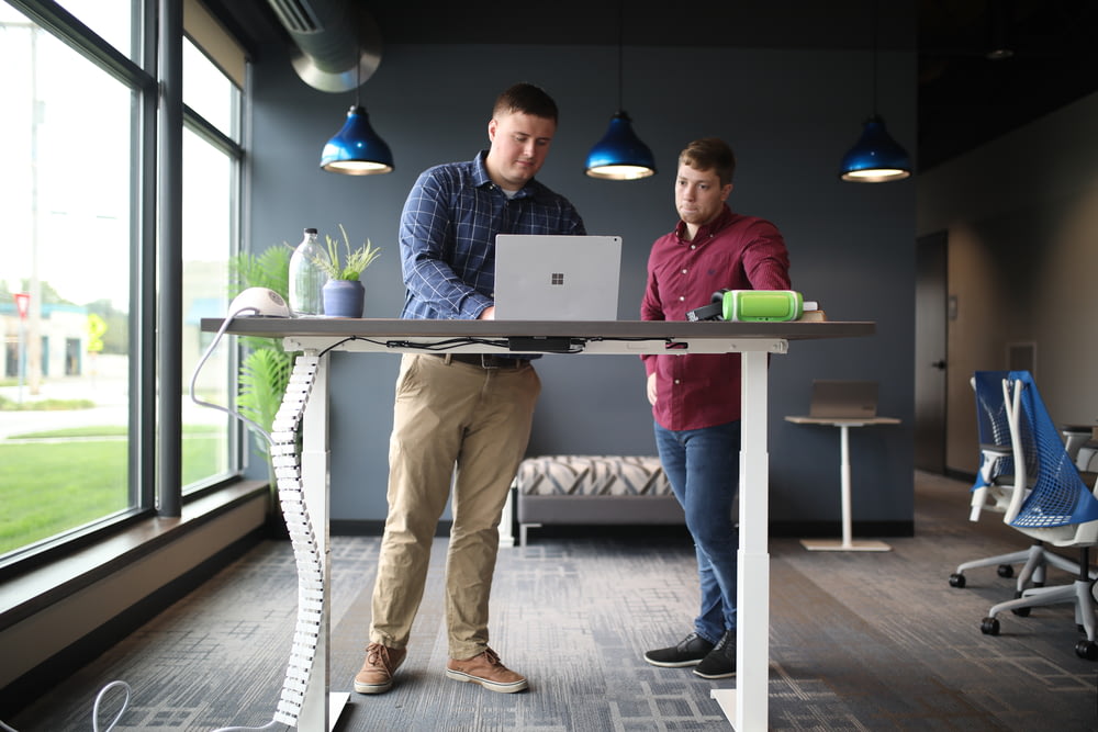 two men standing at a table with a laptop