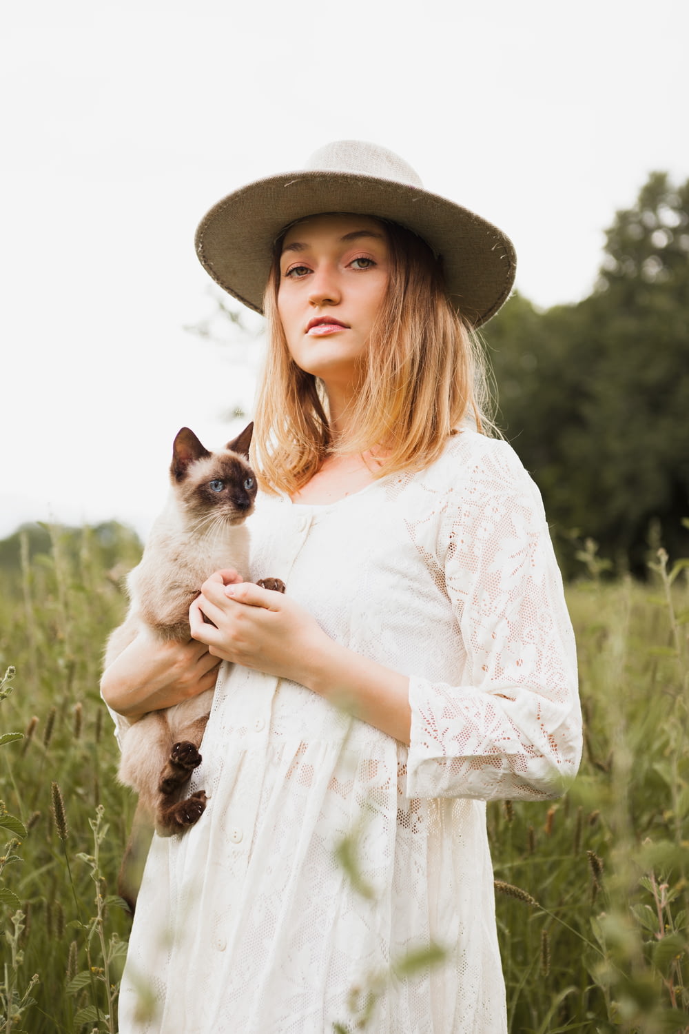 a woman in a hat holding a cat in a field