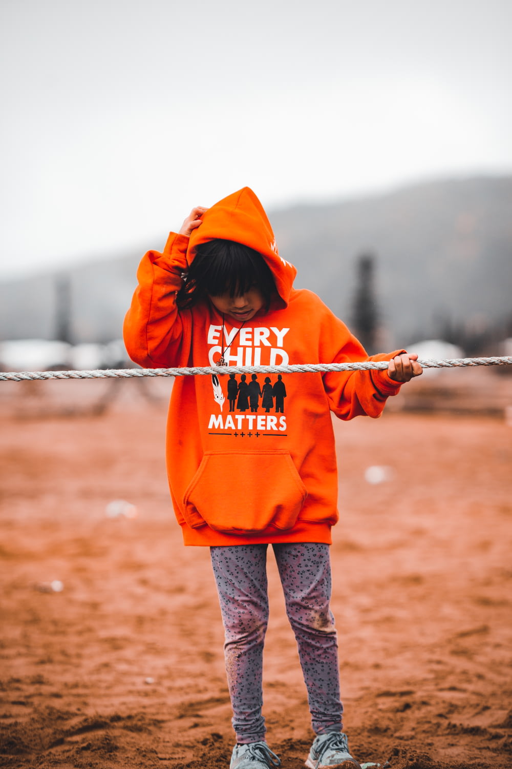 a little girl in an orange hoodie holding a rope