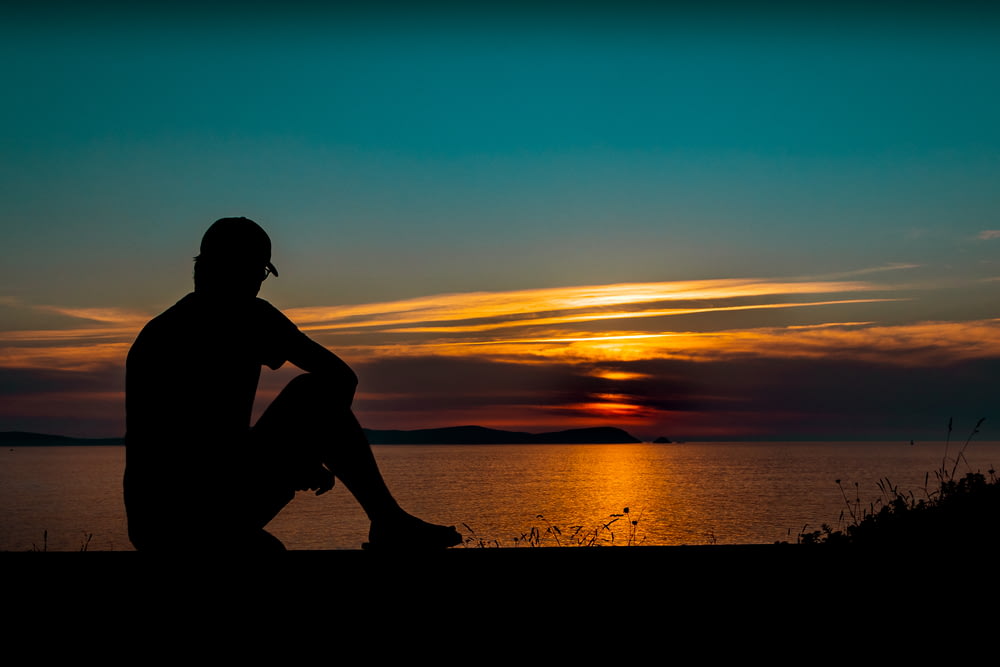 a silhouette of a person sitting in front of a body of water