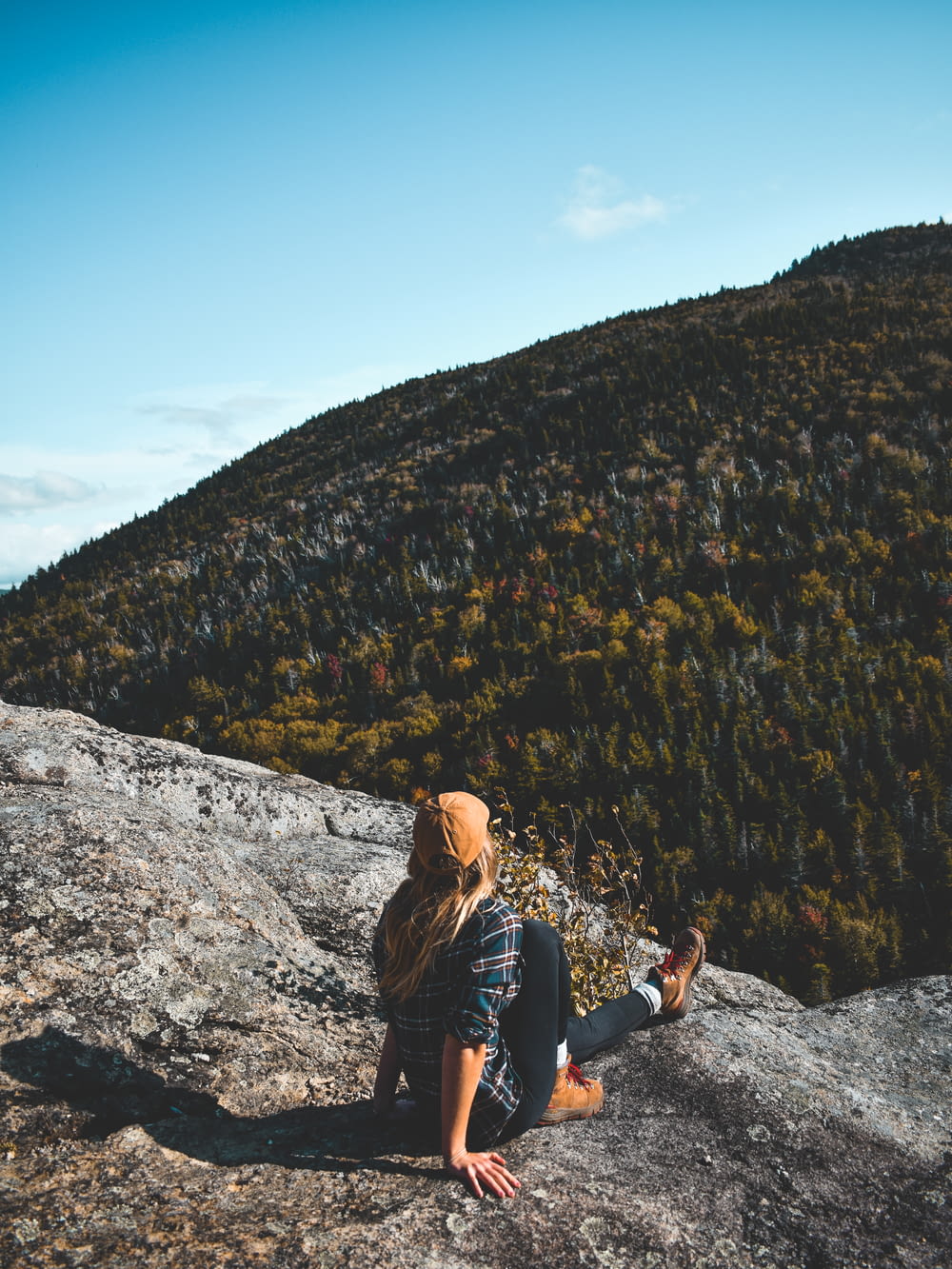 a woman sitting on top of a rock next to a forest