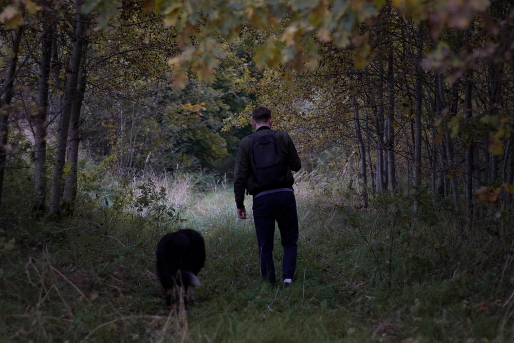 a man walking through a forest with a dog