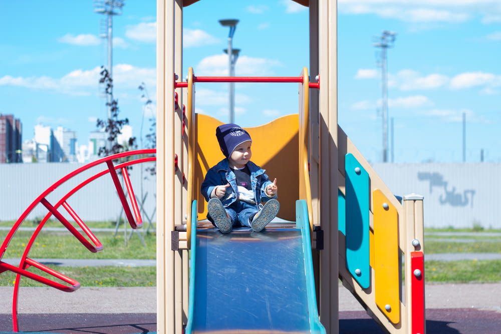 a little boy sitting on a slide at a playground