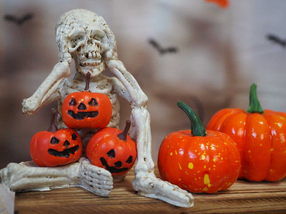 um esqueleto sentado em uma mesa com abóboras
