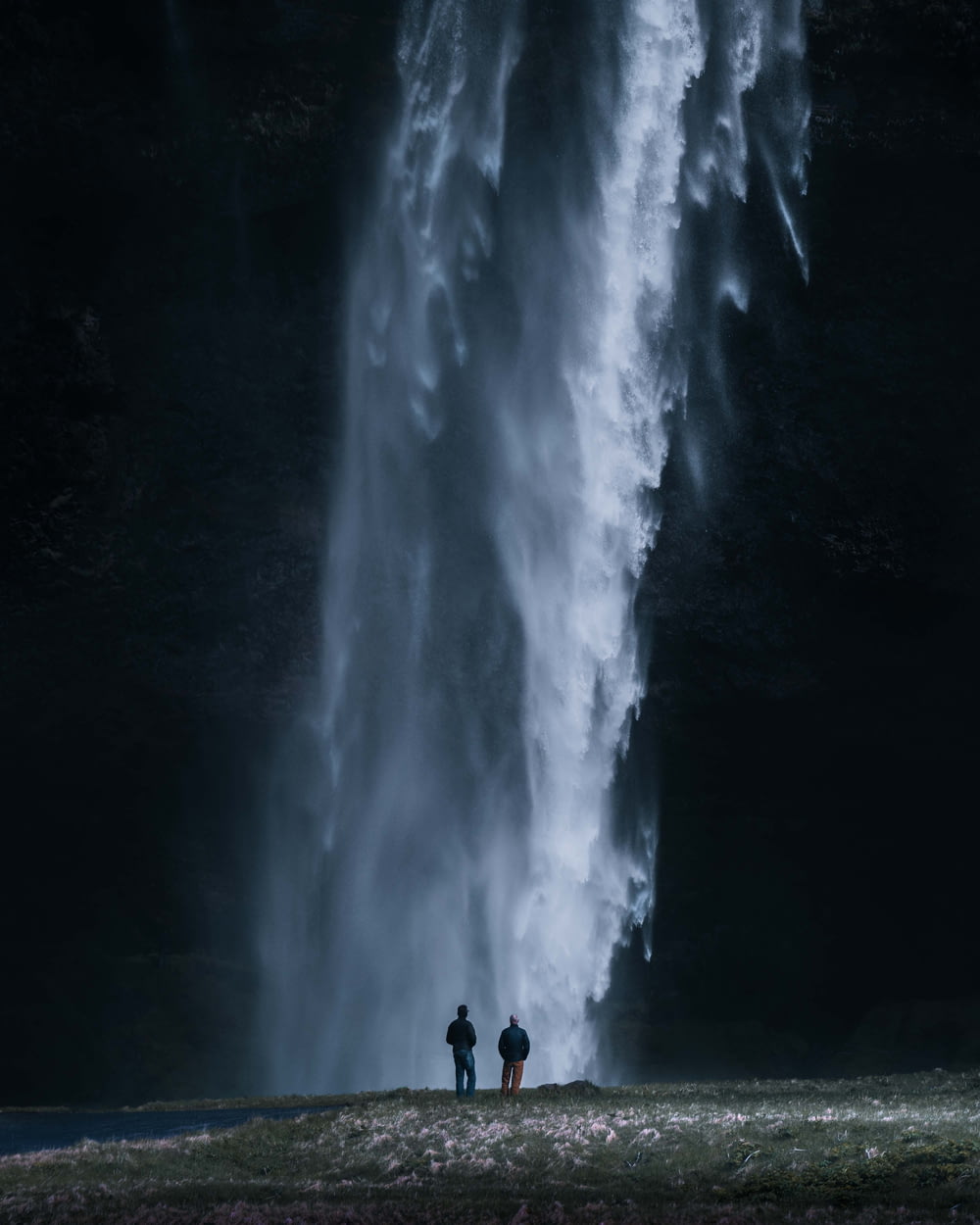 duas pessoas em pé em frente a uma grande cachoeira