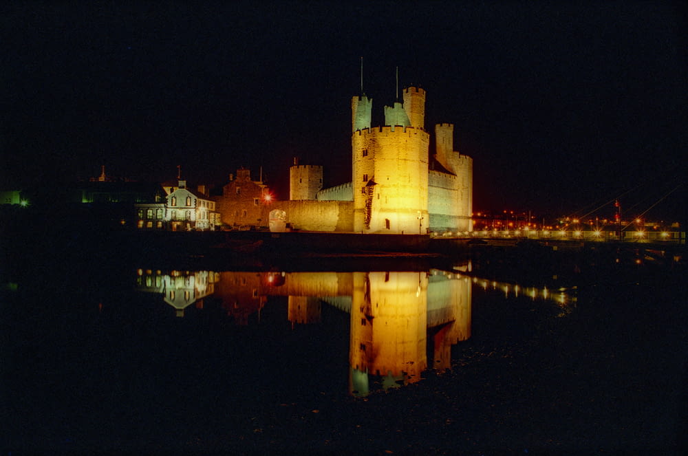a castle lit up at night with a reflection in the water