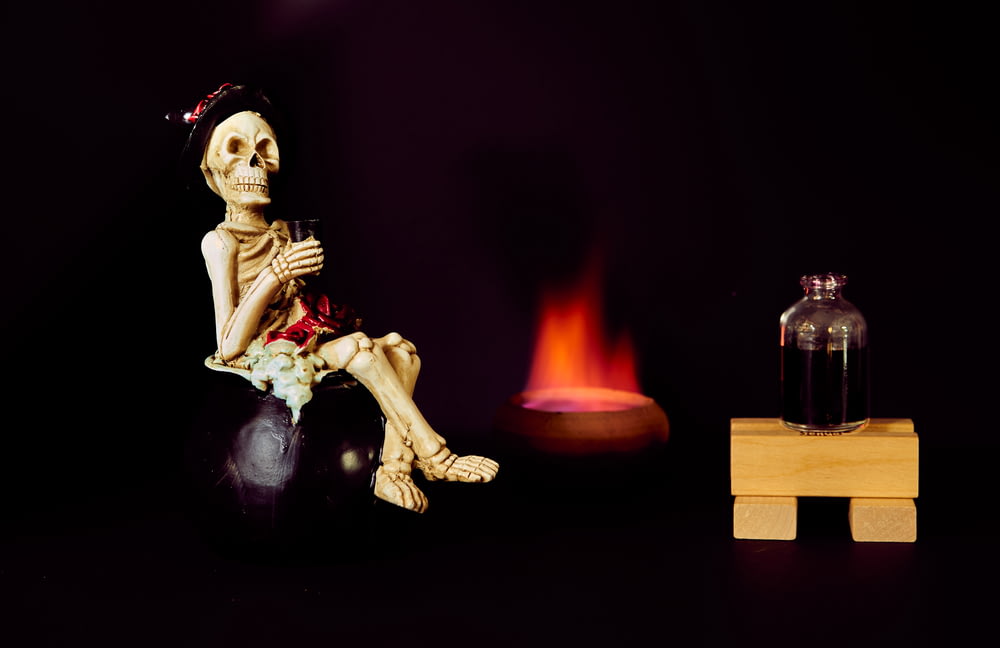 um esqueleto sentado em cima de uma bola ao lado de um fogo