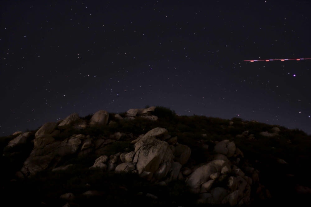 the night sky with stars above a rocky hill