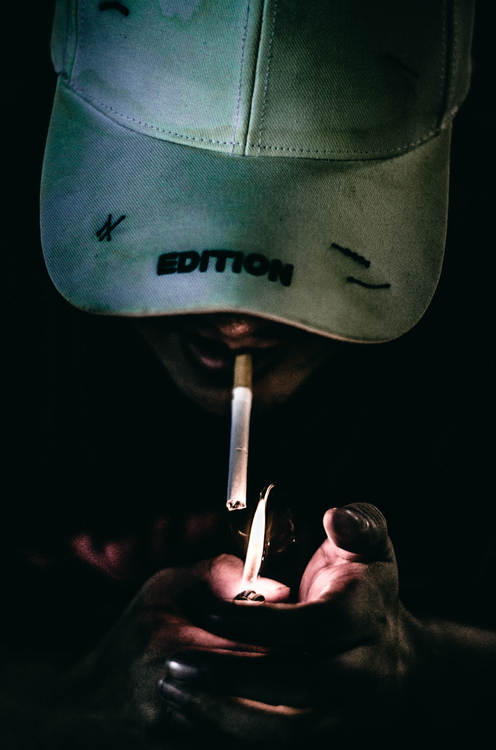 a person lighting a cigarette with a hat on their head