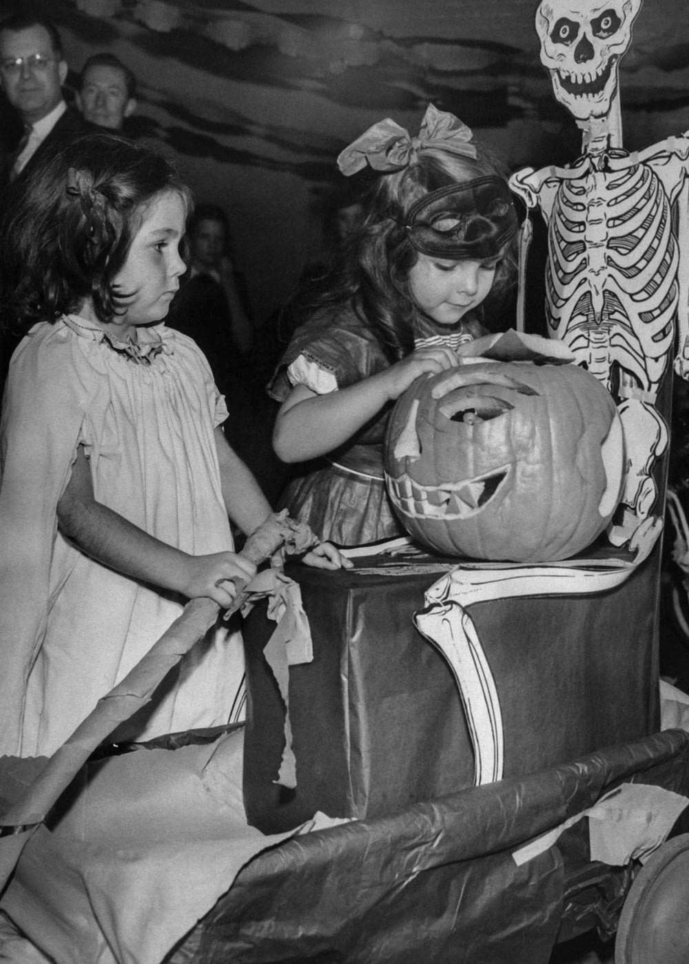 a black and white photo of two girls carving a pumpkin