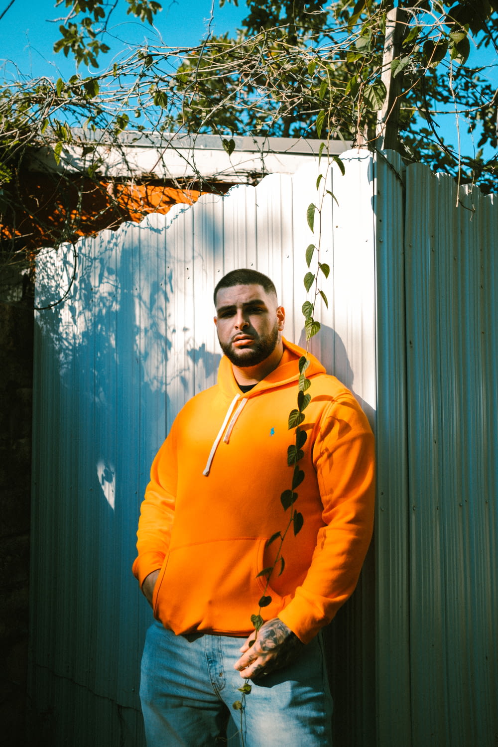 a man in an orange hoodie leaning against a fence