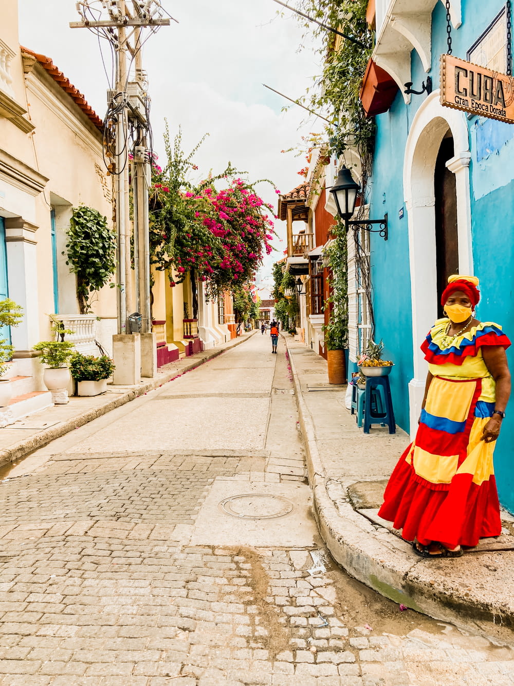 a woman in a colorful dress standing on a cobblestone street