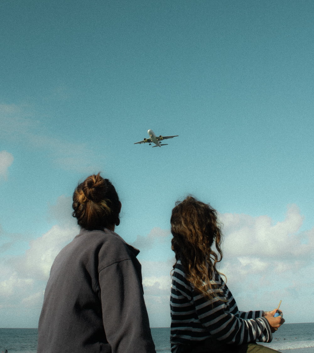 two people looking at an airplane flying over the ocean